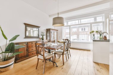 Stüdyo dairesinin modern minimalist tarzı iç tasarımı açık beyaz mutfak ve yemek masası ve sandalyeleri tavan arası lambasıyla aydınlatılmış.