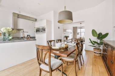 Stüdyo dairesinin modern minimalist tarzı iç tasarımı açık beyaz mutfak ve yemek masası ve sandalyeleri tavan arası lambasıyla aydınlatılmış.