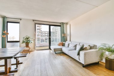 Modern apartmandaki geniş minimalist tarzda oturma odasında halı ve masaya yakın rahat bir kanepe.