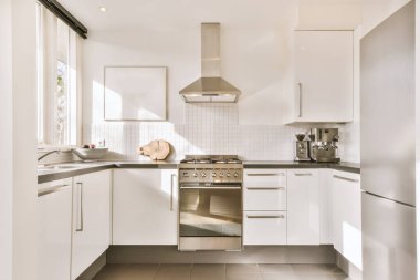 Gündüz vakti modern bir dairede, yemek odasının yakınında modern dolaplar ve aletlerle dolu parlak bir mutfak.