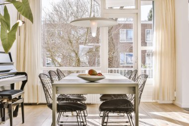 Aydınlık oturma odasının içinde şık mobilyalar, dekorasyonlar, cam kapılar ve güneşli bir günde balkona açılan pencereler.