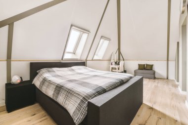 Modern minimalist tarzda, pencereli ve televizyonlu Mansard yatak odasında beyaz duvarın yanına konforlu bir yatak.