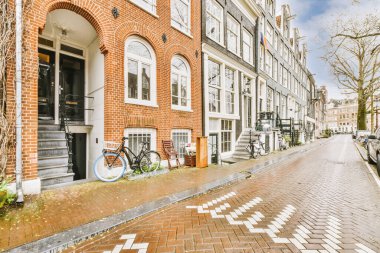 Tabelaları, arabaları, kaldırımları ve ahşap kapıları olan tuğla binanın önü daireye çıkıyor.