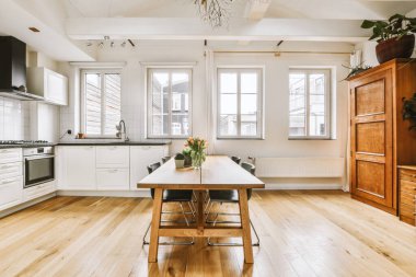 Ahşap masa ve büyük pencereli ve minimalist tasarımı olan modern apartmandaki sandalyeli yemek alanının şık iç tasarımı.