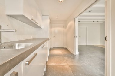 Beyaz duvarları ve fayanslı zemini olan geniş, parlak bir mutfak.