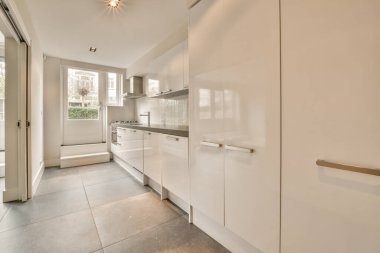 Beyaz duvarları ve fayanslı zemini olan geniş, parlak bir mutfak.