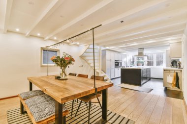 Çağdaş evdeki mutfak ve kapıya parlayan lambaların altına konmuş sandalyeli ve çiçekli masa.