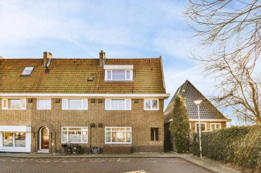 Bisikletli, fenerli, kaldırımlı ve ahşap kapılı tuğla binanın önü.