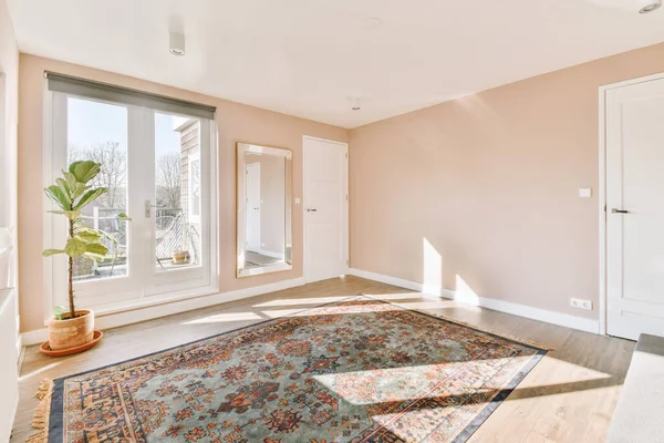 Persian carpet on the parquet floor in the room flooded with sun through the door to the balcony and