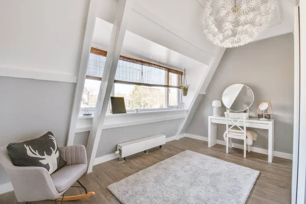 Bright attic room with a window, an armchair and a dressing table and a stylish chandelier