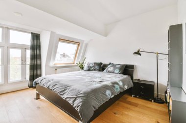 Beyaz duvarlı, siyah yataklı, beyaz tavanlı, sade bir yatak odası.