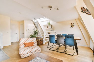 Çağdaş dairenin geniş odasındaki dinlenme odası ve mutfağın yakınındaki sandalyeli ve çiçekli masa.