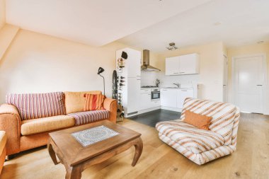 Çağdaş dairenin geniş odasındaki dinlenme odası ve mutfağın yakınındaki sandalyeli ve çiçekli masa.