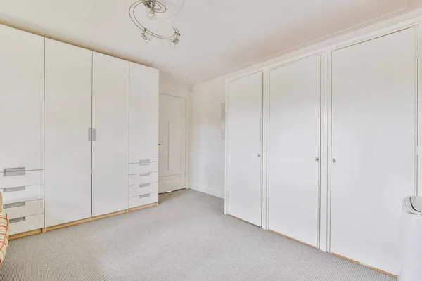 A white empty room with storage space and wardrobes, with a stylish chandelier in the center of the ceiling.om with wardrobes