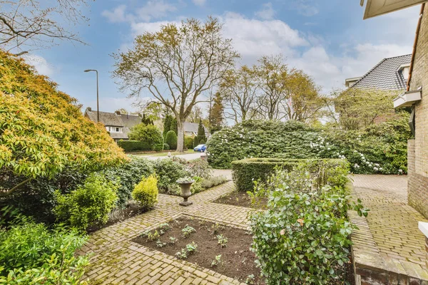 View of flower beds, bushes near the house and neighboring brick houses and trees