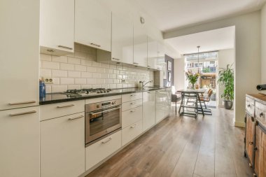 Beyaz duvarları ve parke zemini olan geniş, parlak bir mutfak.