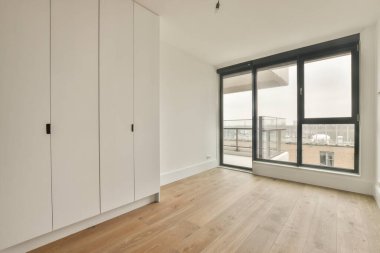 Modern dolap ve klasik sandık, beyaz duvarları ve ahşap zemini olan geniş bir odada, kapıların ve hasır sepetin yanına yerleştirildi.