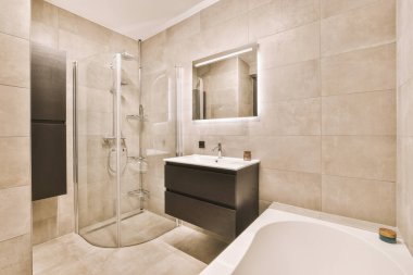 Aynalı lavabo ve temiz küvet modern banyoda cam kapılı ve beyaz fayanslı duvarları olan duş kutusunun yanında.