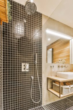 Küvetli modern banyo ve ışıklı cam duş kabini ve aynalı lavabo, bej fayans ve beyaz tavan.