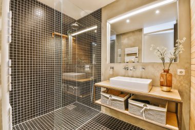 Küvetli modern banyo ve ışıklı cam duş kabini ve aynalı lavabo, bej fayans ve beyaz tavan.