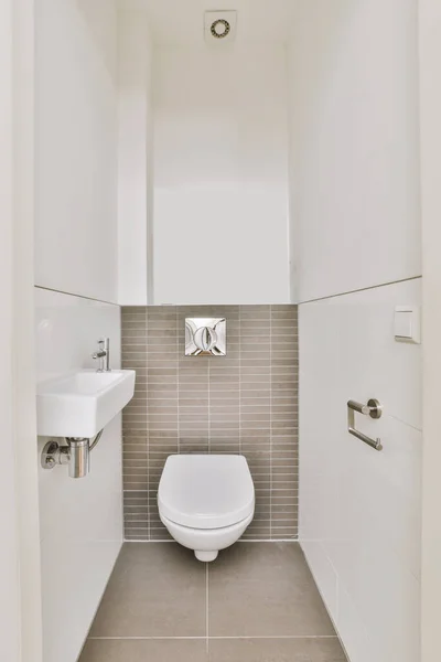ボタンの下のベージュの壁には現代的なトイレが設置され 自宅の軽いトイレには小さなセラミックシンクが設置されています — ストック写真