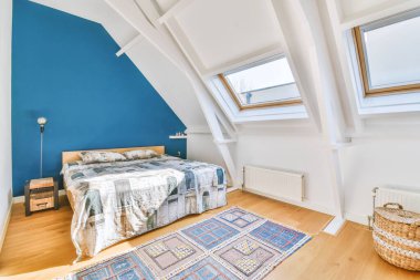 Çatı katındaki mavi duvarın yanında rahat bir yatak odası modern minimalist tarzda pencereli.