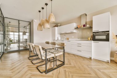 Çağdaş dairenin geniş odasındaki dinlenme odası ve mutfağın yakınındaki sandalyeli ve çiçekli masa.