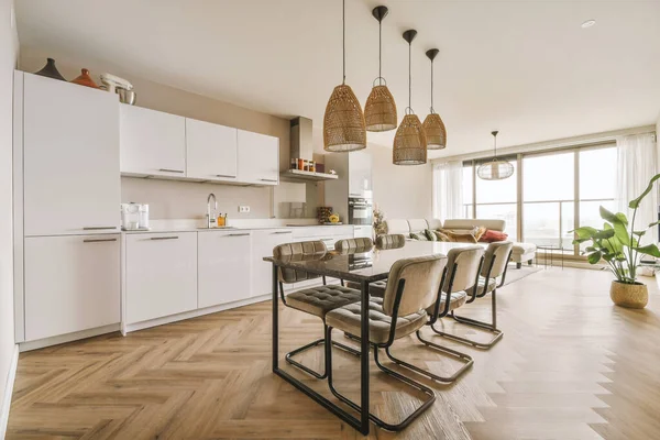 Çağdaş dairenin geniş odasındaki dinlenme odası ve mutfağın yakınındaki sandalyeli ve çiçekli masa.