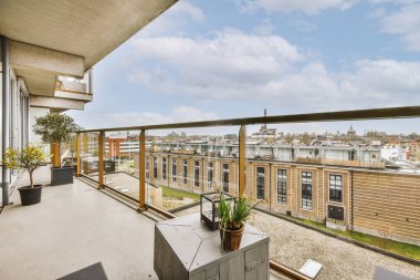 Metal parmaklıklı dar tuğla balkon, tahta sandalye ve camlı kapı mutfağa açılıyor.