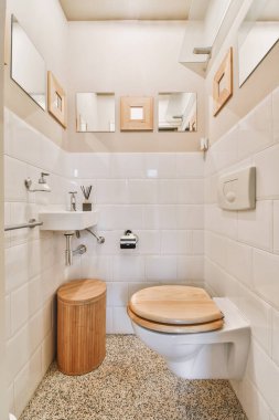 Duvara asılmış tuvalet ve köşedeki bej fayanslı lavabo.