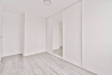 Ayna ve ahşap parke zeminli büyük dolabı olan boş beyaz bir oda.