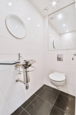 Lavabosu ve duvarı olan, beyaz duvarlı, kareli zemini ve iki aynası olan dar bir tuvaletin içi.