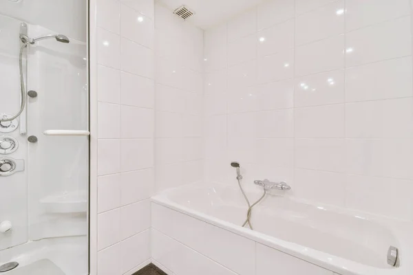 バスタブとガラスシャワーキャビン付きの現代的なバスルームには 薄い白いタイルと暗い天井 — ストック写真