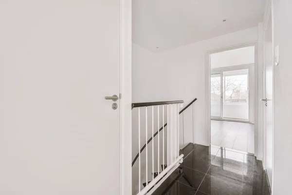 Light hallway with entrance door in two level apartment with minimalist metal staircase leading downstairs in daylight