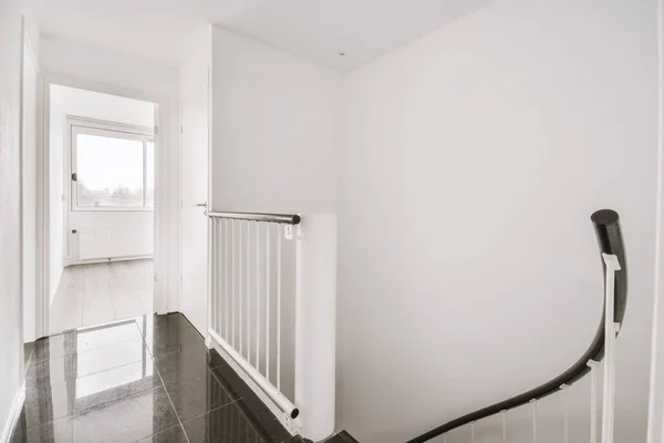 Light hallway with entrance door in two level apartment with minimalist metal staircase leading downstairs in daylight