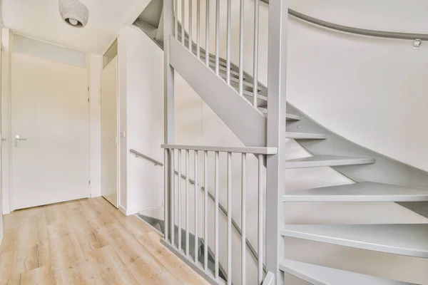灰色螺旋形楼梯将现代房屋的各个楼层与木制地板和白色墙壁连接起来 — 图库照片