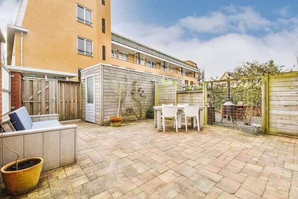 Masası, sandalyeleri ve küçük ahşap ek binası olan düzgün asfaltlı bir teras.