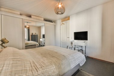 Yatak odasının iç tasarımı, yatak odası ve ahşap gardırop. Modern apartmanın penceresinin kenarına televizyon yerleştirilmiş.