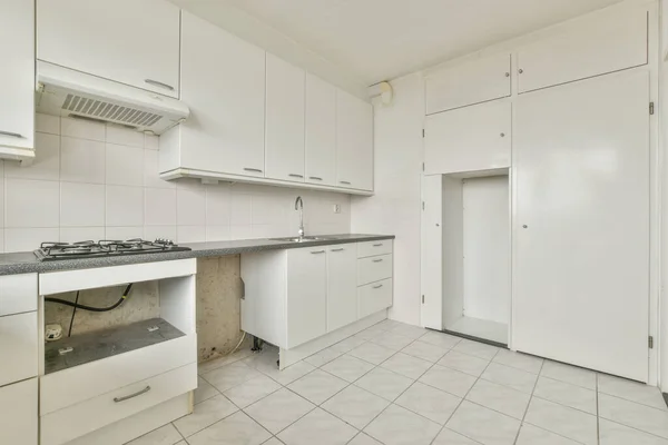 シンクとストーブ付きのミニマリストスタイルの白い家具と光の狭い家庭用キッチンの内部の断片 — ストック写真