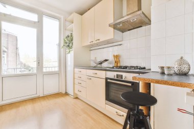 Gündüz vakti ahşap zemin, dolaplar ve balkon kapıları olan parlak bir mutfak.