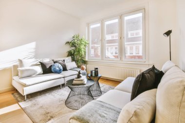 Geniş pencereli, beyaz duvarlı, rahat kanepe ve halı döşeli, geniş oturma odasının şık iç tasarımı.