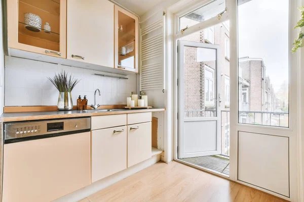 Interior of a bright kitchen with beige furniture and balcony doors in a modern apartment