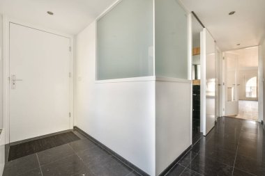 Beyaz duvarları ve kapıları olan dar koridor modern dairede pencereleri ve parke zemini olan geniş odaya açılıyor.