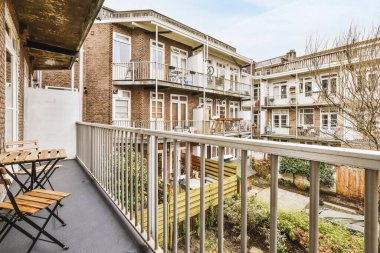 Dar tuğlalı balkon, metal parmaklıklar, tahta sandalye ve kapı.