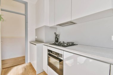 Hafif, dar bir ev mutfağının bir parçası. Fırında soba olan minimalist tarzda beyaz mobilyaları var.