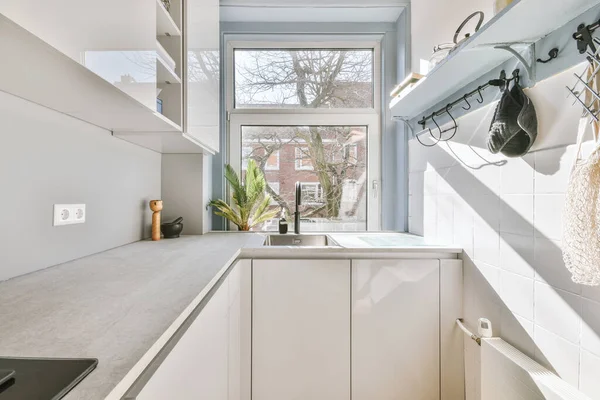 Well organized interior of a small home kitchen with a sink under the window and light furniture with a stove and a radiator in a city apartment