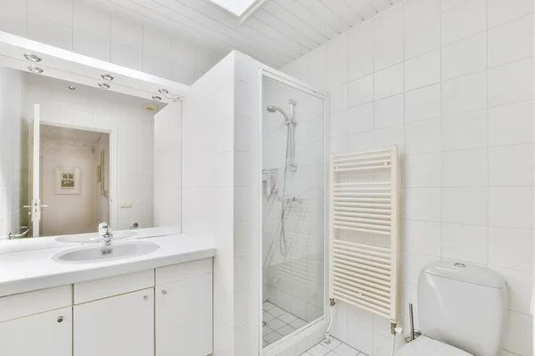 シャワーボックスの近くの白いタイル張りの壁に設置された現代のフラッシュトイレとセラミックシンクと自宅の小さなトイレでタオル — ストック写真