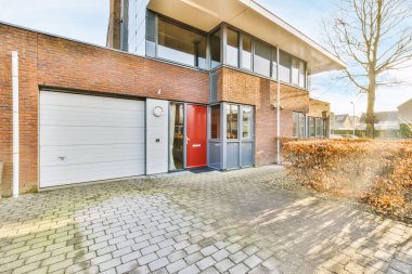 Tabelaları, arabaları, kaldırımları ve ahşap kapıları olan tuğla binanın önü daireye çıkıyor.