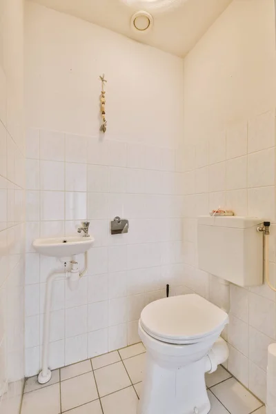 家の小さなトイレに白いタイル張りの壁に設置された現代のフラッシュトイレとセラミックシンク — ストック写真