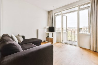 Modern minimalist tarzı oturma odasının iç tasarımı. Büyük pencereleri ve beyaz duvarlı ahşap kanepesi var.